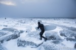 Gart Curtis runs back up the beach over big chunks of ice in a snow blizzard while surfing Ninilchik, Alaska in winter.